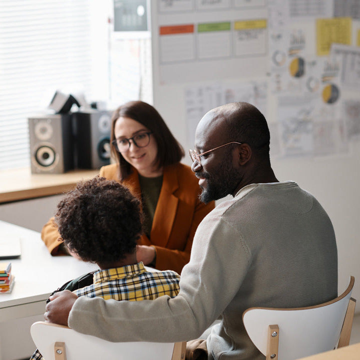 Three people sitting around a table in an office setting with a whiteboard in the background.